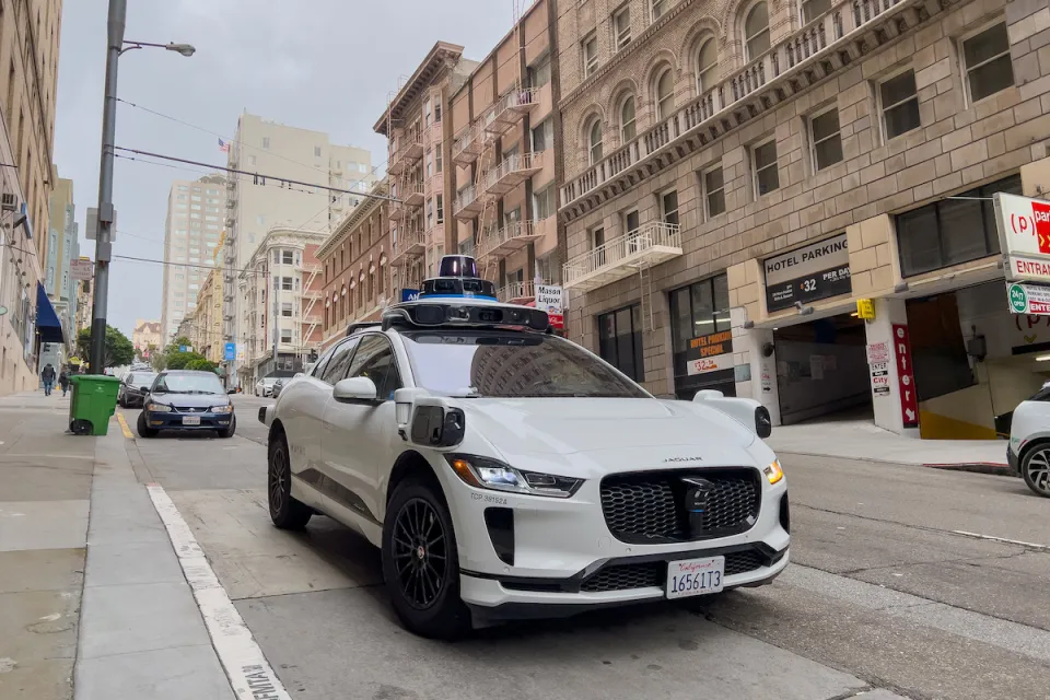 White Waymo self-driving taxi on street in San Francisco, California with brick buildings in background.